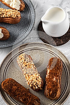 Two plates with homemade eclairs and white cream bowl on the table, glazed patisseries with milk drink photo