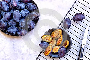 Two plates of whole and cut ripe blue plums on white marble background. Top down view. Close-up. Flat lay composition