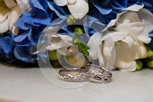 Two platinum wedding rings lie bouquet of blue and white flowers.