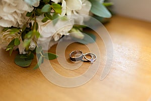 Two platinum wedding rings on wood background with flowers. Bride ring with diamonds. Shallow focus. Rustic wed concept