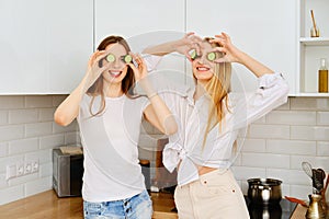 Two playful women put pieces of cucumber to their eyes