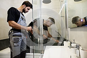 Two plumbers, workers in uniform working, fixing water tap in bathtub using wrench and sticky tape indoors. Repair