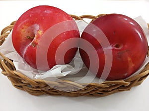 two plums in a small basket on a white background