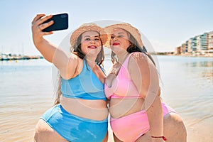 Two plus size overweight sisters twins women happy taking a selfie picture at the beach on summer holidays