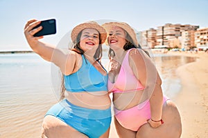 Two plus size overweight sisters twins women happy taking a selfie picture at the beach on summer holidays