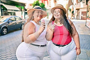 Two plus size overweight sisters twins women smiling eating an ice cream outdoors