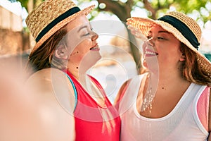 Two plus size overweight sisters twins women smiling taking a selfie picture with the phone outdoors