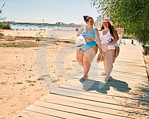 Two plus size overweight sisters twins women walking at the beach on summer holidays