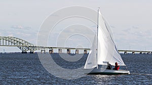 Two poeple on a small sailboat in the winter with the great south bay bridge in background