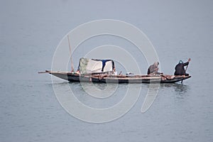 Two poor fishermen rowing old wooden row boat to catch fish in the padma river, Bangladesh