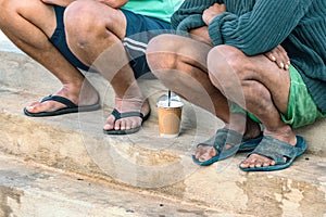 Two port workers taking a break sitting with sandals on their feet and having cold coffee in Heraklion, Greece