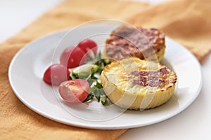 Two portioned round-shaped baked omelette, halves of cherry tomatoes, chopped green onions on white plate.