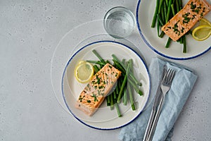 Two portions of baked salmon with asparagus, lemon and parsley. Glass of water. Overhead