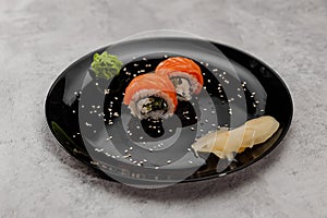 Two portions of sushi with salmon and cucumber with vossabi sauce and ginger on a black plate.