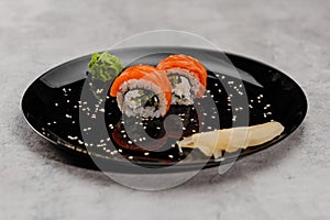 Two portions of sushi with salmon and cucumber with vossabi sauce and ginger on a black plate.