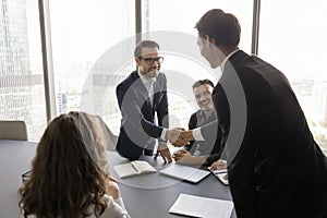 Two positive business leader men shaking hands on group meeting