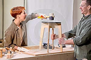 Two positive carpenters making wooden chair in workshop, team work