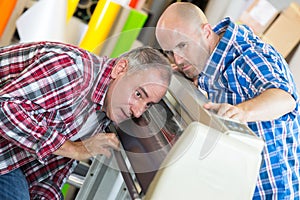 Two positive cheerful workers working on machine