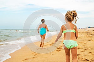 Two positive little girls run along sandy beach