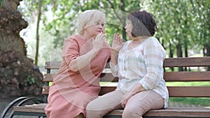 Two positive senior girlfriends gossiping and sharing secrets. Portrait of Caucasian women sitting on bench in summer