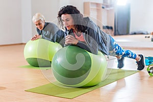 Two positive women doing plank exercise lying on balance ball in gym photo