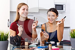 Two positive young female friend choosing cosmetics make up at table