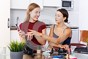 Two positive young female friend choosing cosmetics make up at table