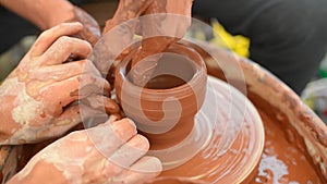 Two potters with his hands are shaping a clay pot rotating on a potter`s wheel