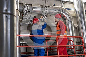 Two Power Plant Workers in Personal Protective Equipment Turning the Valve on Industrial Piping