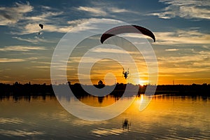 Two powered paragliders flying over the lake during sunrise. Paramotor pilot with reflection in the water