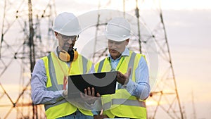 Two powermen are talking outside near electrical towers