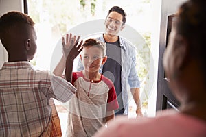 The two pre-teen boys high five in the open doorway, as dad drops his son off at his friendsï¿½ house
