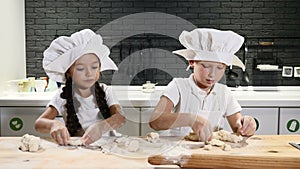 Two preschool kids working side by side cooking pies and cookies. Children chefs wear hats and aprons. 6-7 year old guys