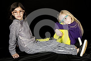 Two preteen girls sitting on ground wearing fun eye glasses