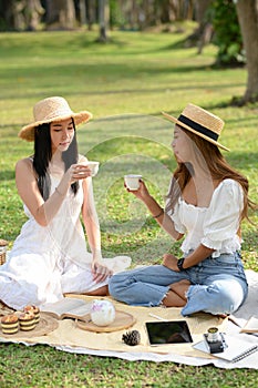 Two pretty Asian women having an afternoon tea picnic in the greenery park