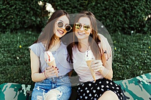 Two pretty brunette girls talking and eating ice cream outdoor on the grass