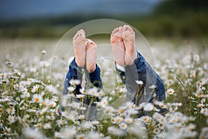 Two pretty child girls are lying down with feets up at camomile field