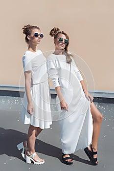 Two pretty cute fashion girl girlfriends in white gowns posing for fashion clothing catalog in sunglasses on a bright sunny summer