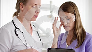 Two pretty female doctors discussing something on tablet at hospital room. Medical staff at work