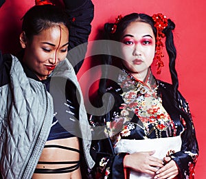 two pretty geisha friends: modern asian woman and traditional wearing kimono posing cheerful on red background