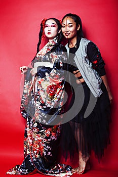 Two pretty geisha girls friends: modern asian woman and traditional wearing kimono posing cheerful on red background