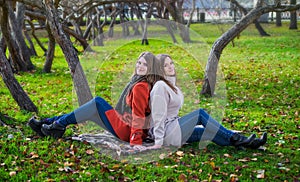 Two pretty girlfriends are sitting on lawn in park