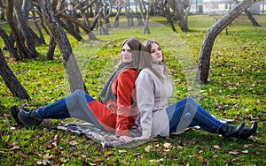 Two pretty girlfriends are sitting on lawn in park