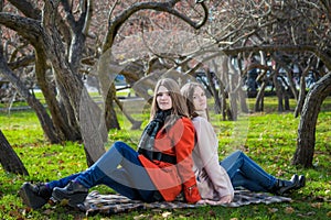 Two pretty girlfriends are sitting on lawn in park