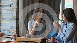 Two pretty girlfriends talk and drink tea in cafe