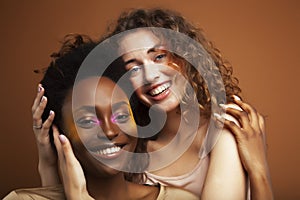 Two pretty girls african and caucasian blond posing cheerful together on browm background, etnithity diverse lifestyle