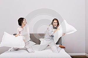 Two pretty girls having pajamas party. They fighting with pillow fight on bed.