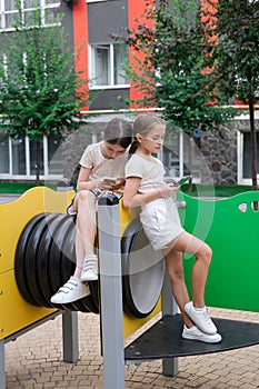 two pretty girls in identical clothes using phone on sports ground or athletic field. kids are surfing in internet