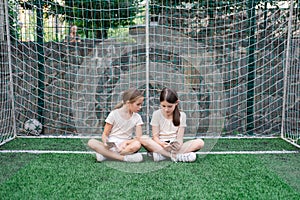 two pretty girls in identical clothes using phone on sports ground or athletic field. kids are surfing in internet