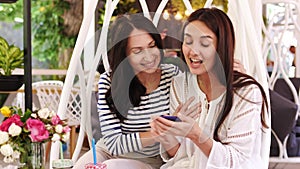 Two pretty girls are laughing during look over photos on phone sitting at cafe